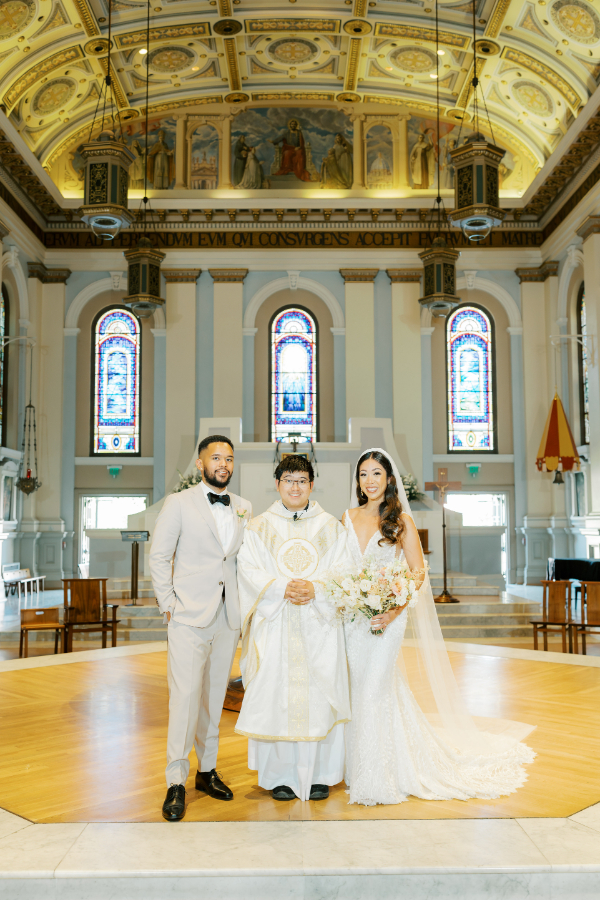 Bride and groom stand with the Catholic priest from their Cathedral Basilica of St. Joseph wedding ceremony