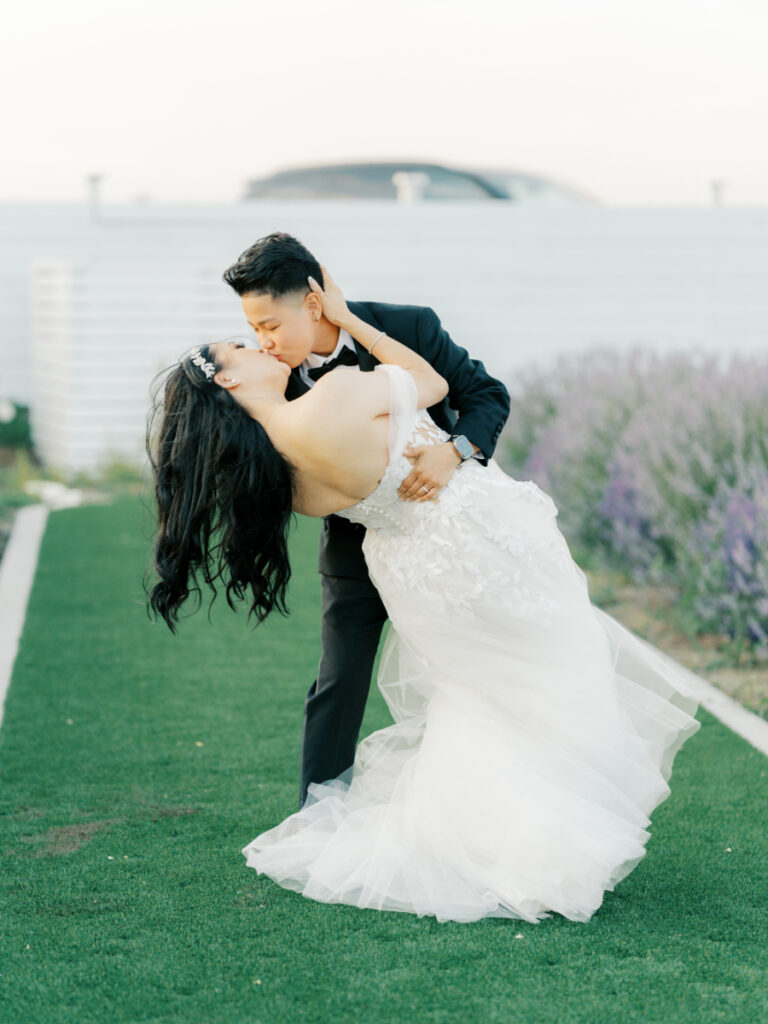 San Francisco groom dips bride in a greenspace amidst purple flowers wearing San Francisco bridal shop find