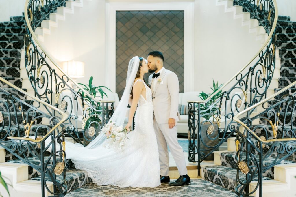 Bride and groom kiss at the bottom of a grand staircase while bride holds a bouquet during Silver Creek Country club wedding 